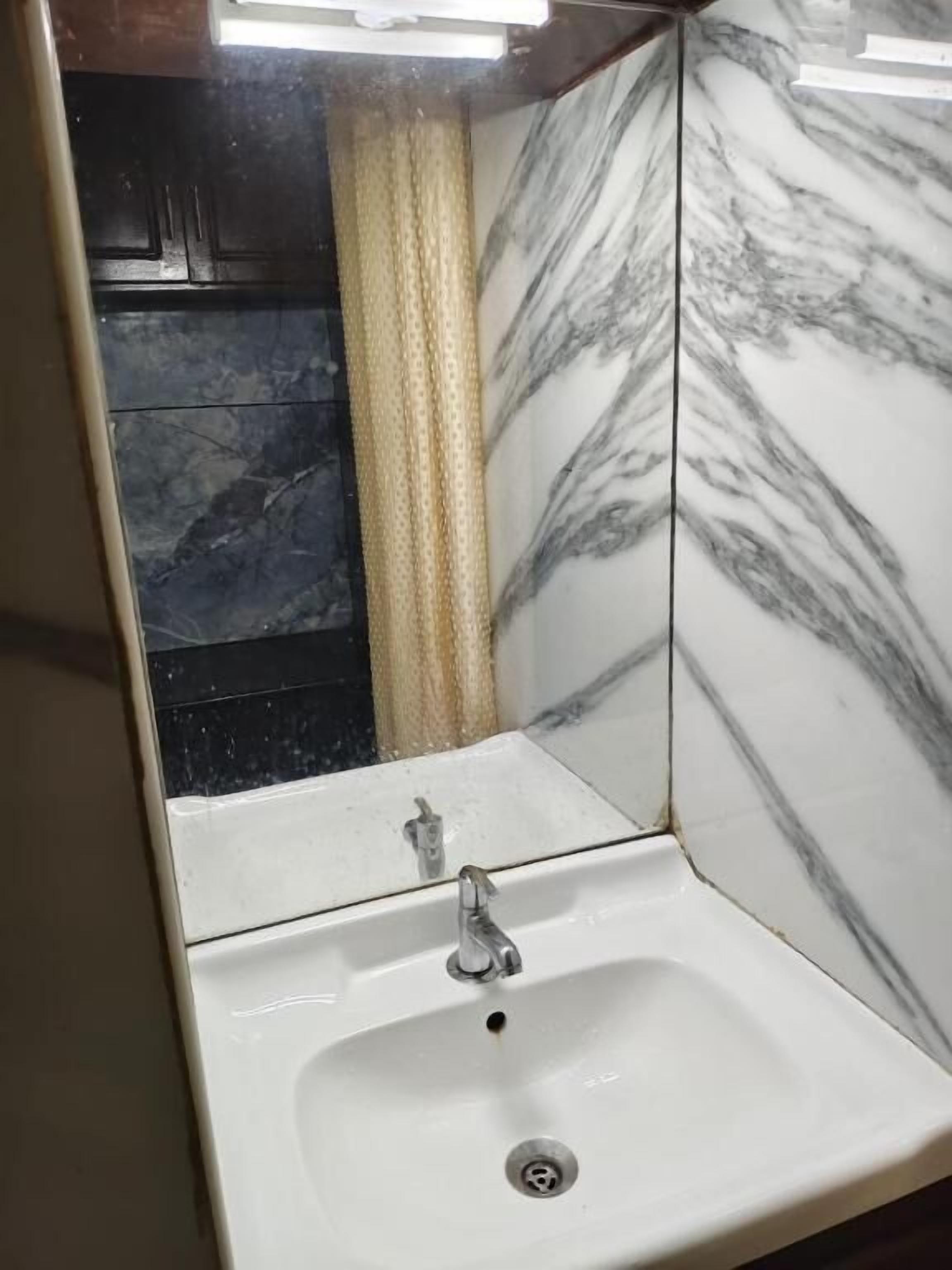A bathroom with a white sink, marble walls, and a shower area.