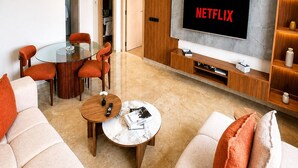 Una sala moderna con un televisor de pantalla plana grande, un comedor con sillas color naranja y un mueble de madera con un letrero de Netflix.