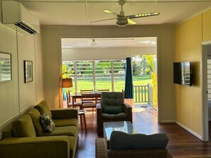 A living room with a sofa, armchair, and coffee table, a television, and a ceiling fan. - Kooyong Aprtments (Arcadia)