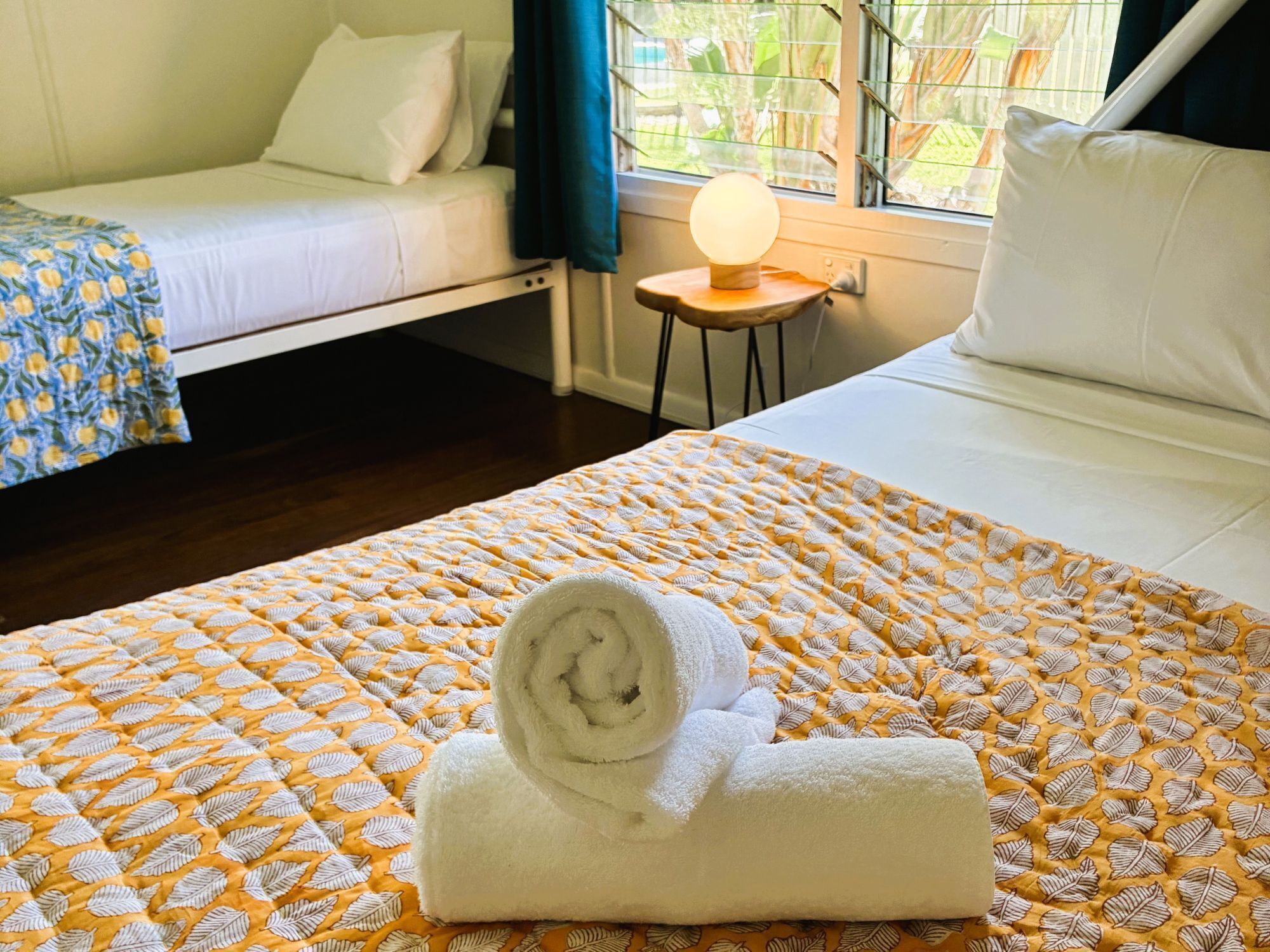 A hotel room with a bed, a smaller bed, a window with a view, and a bedside table with a lamp.