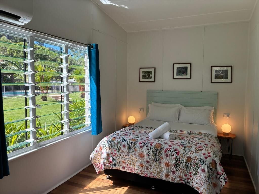 A bedroom with a bed, a window with a view of greenery, and three framed pictures on the wall.