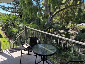 Un balcone con un tavolo e sedie in vetro, immerso nel verde e alberi.
