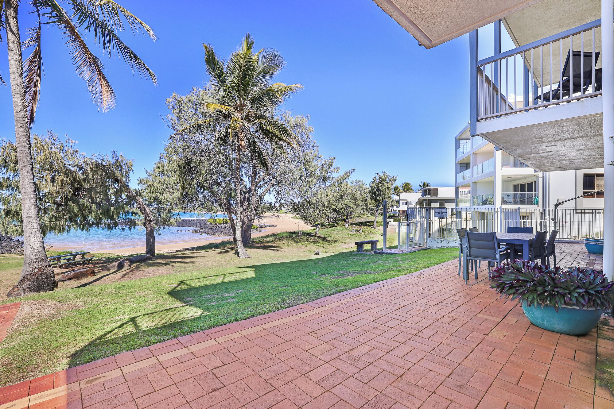 A patio with a view of the beach, palm trees, and a building with balconies.