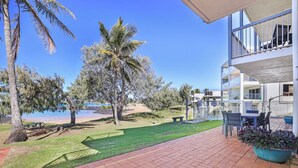 A patio with a view of the beach, palm trees, and a building with balconies. - 2 Bedroom Unit with Beach & Golf at your doorstep! (Bargara)