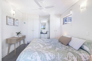 Quarto com cama, escrivaninha, guarda-roupa e ventoinha no teto.