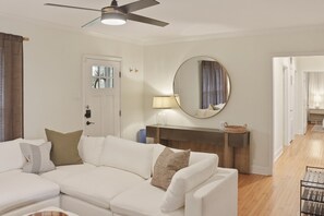 A modern living room with a sectional sofa, a ceiling fan, a round mirror, and a wooden console table. - Real Home Near UT & Downtown - 3 Bed 2 Bath, Big Yard, Great Design (Austin)