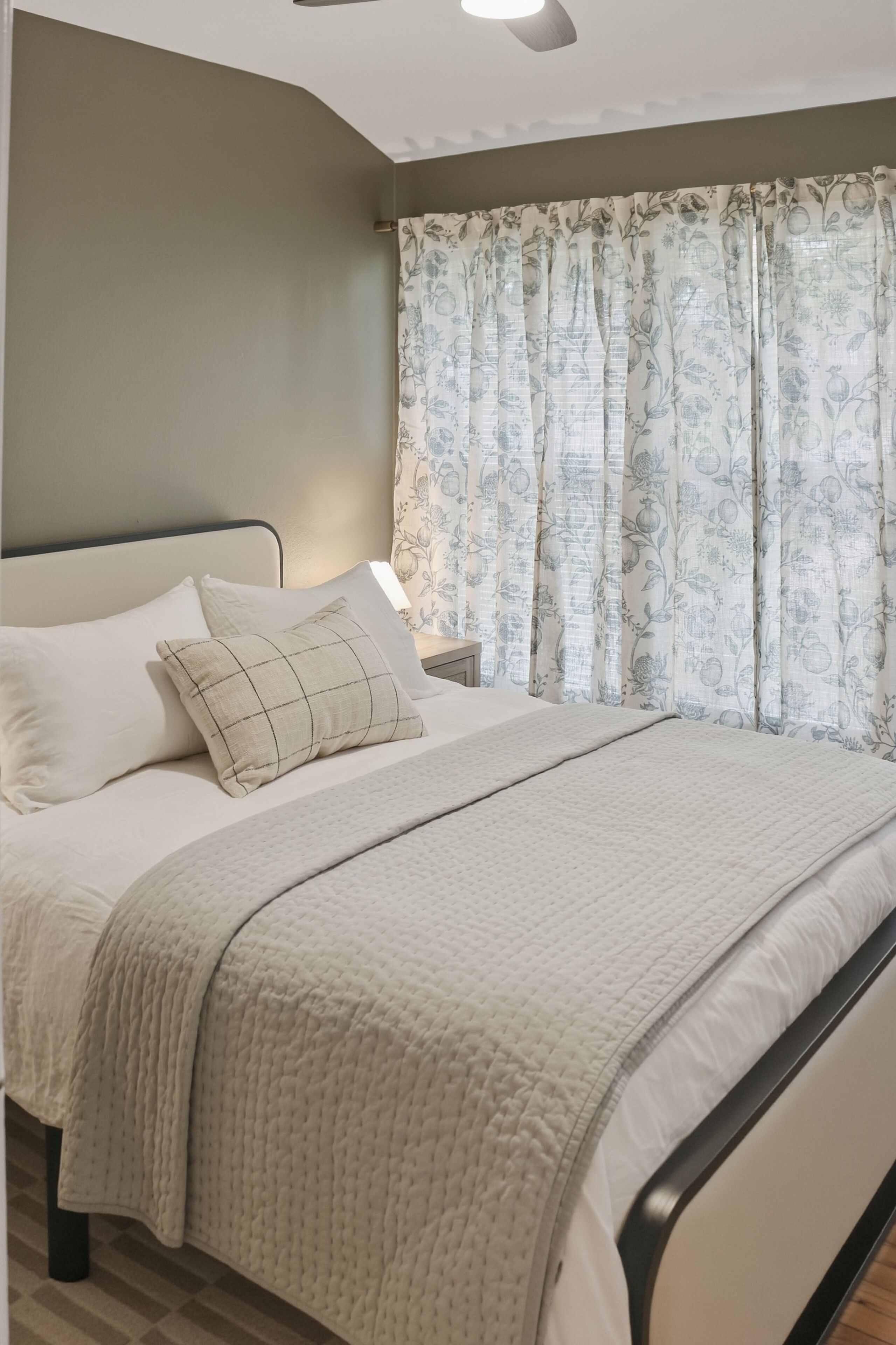 A neatly made bed with a quilted blanket, a pillow, and a bedside table with a lamp.