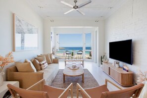 Ein geräumiges Wohnzimmer mit großem Fernseher, einer Couch, einem Couchtisch und Blick auf den Strand.