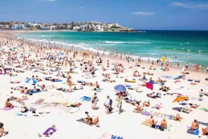 A crowded beach with people sunbathing and swimming, and buildings in the background. - Deluxe Bondi Suite - AC Laundry (Bondi Beach)
