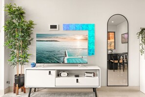 A modern living room with a large TV, a white cabinet, a potted plant, and a view of the sea. - Stylish & Spacious Modern 1 BDR Balcony BBQ AC (Bondi Beach)