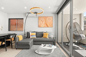 Un salon moderne avec un canapé gris, une table basse blanche, un fauteuil suspendu et une grande fenêtre.