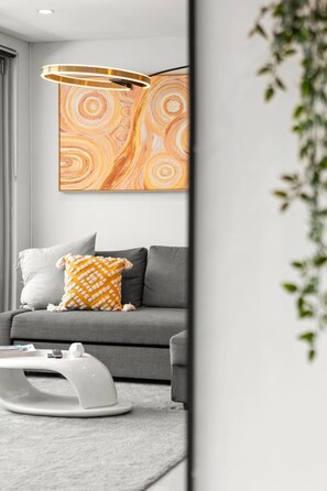 Un salon moderne avec un canapé gris, une table basse blanche et un luminaire mural original.
