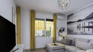 Una sala moderna con televisor de pantalla plana, un sofá, una mesita de centro, una lámpara y un cuadro en la pared.
