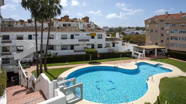 Una piscina rodeada de césped cuidado, con vistas a edificios residenciales al fondo.