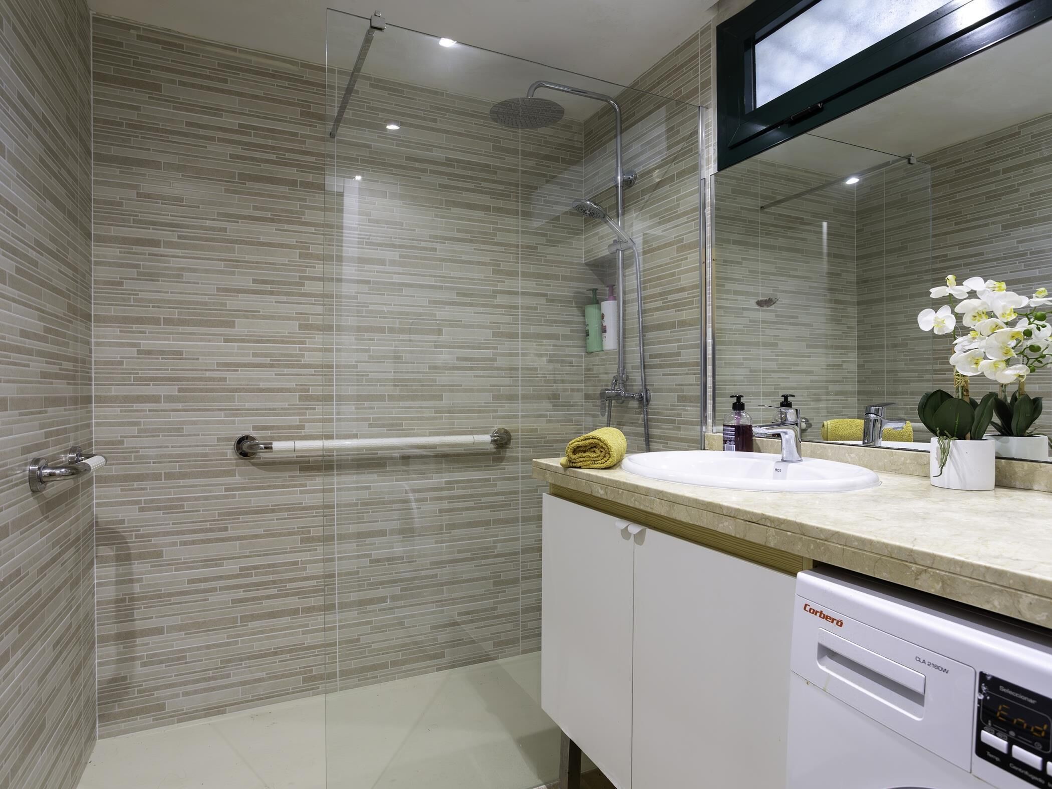 Une salle de bain moderne avec une douche à parois de verre, un lavabo blanc et un lave-vaisselle Corbero.