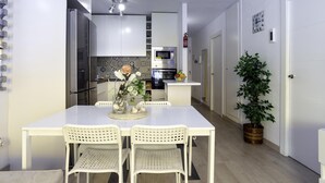 Una cocina moderna con armarios blancos, un microondas y un horno. Hay una mesa de comedor con dos sillas, un jarrón con flores y una planta en maceta.