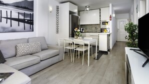 Una sala de estar moderna con sofá, una mesa de comedor con sillas, una cocina con armarios y electrodomésticos, y un amplio ventanal con vistas.