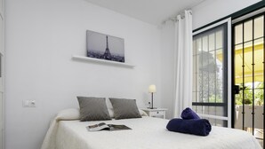 Un dormitorio con cama, almohadas, una mesita de noche, lámpara, ventana con cortinas, y una imagen de la Torre Eiffel.