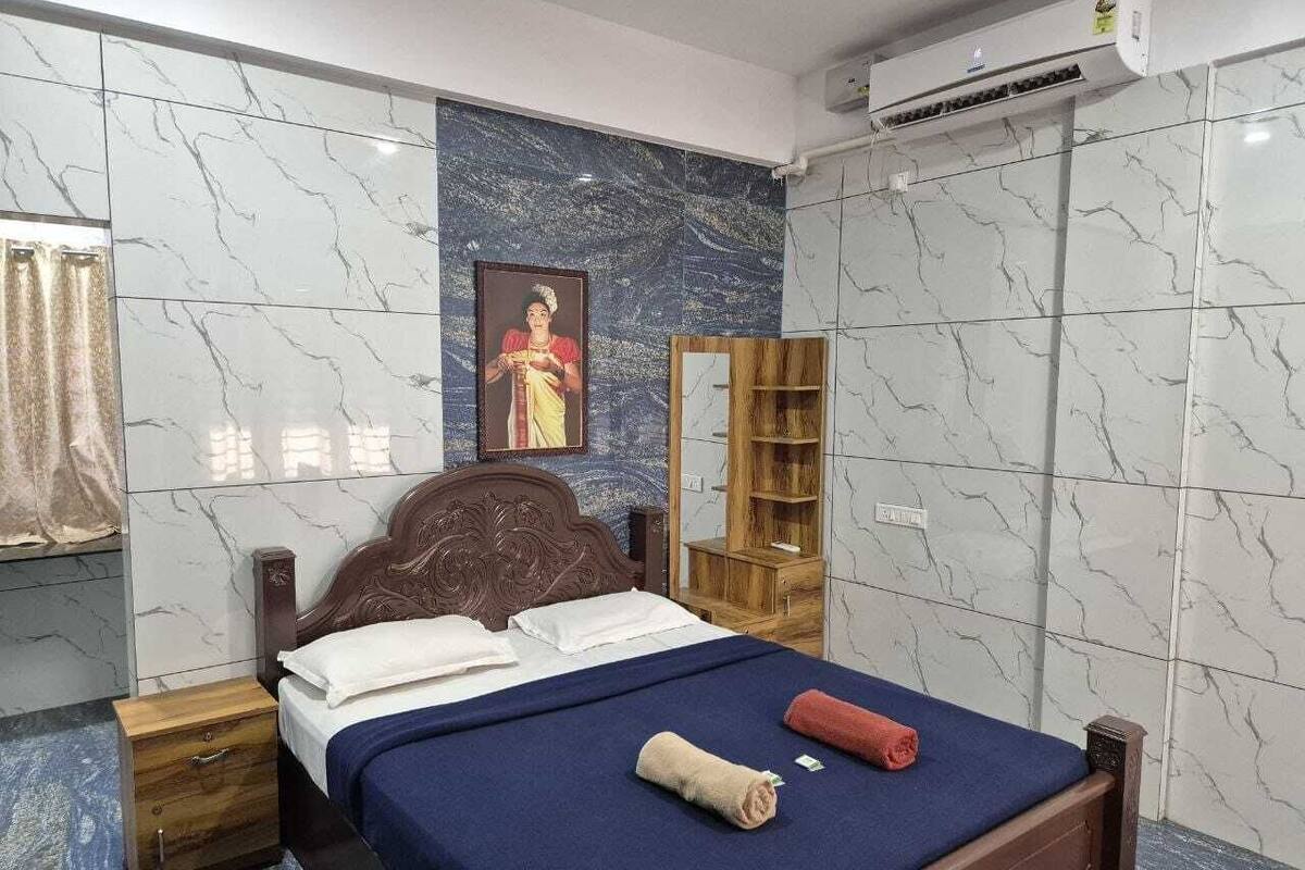A bedroom with a bed, wooden nightstands, a wardrobe, a mirror, and an air conditioning unit.