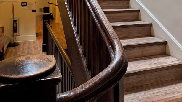 Una scala in legno con corrimano, un tavolo rotondo e un cartello che indica gli orari di silenzio.