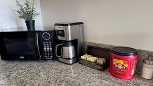 Una cucina con forno a microonde, macchina del caffè e un barattolo di caffè Folgers.