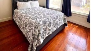 Una camera da letto con testiera trapuntata, copriletto decorato, ventola a soffitto e finestra con tende.