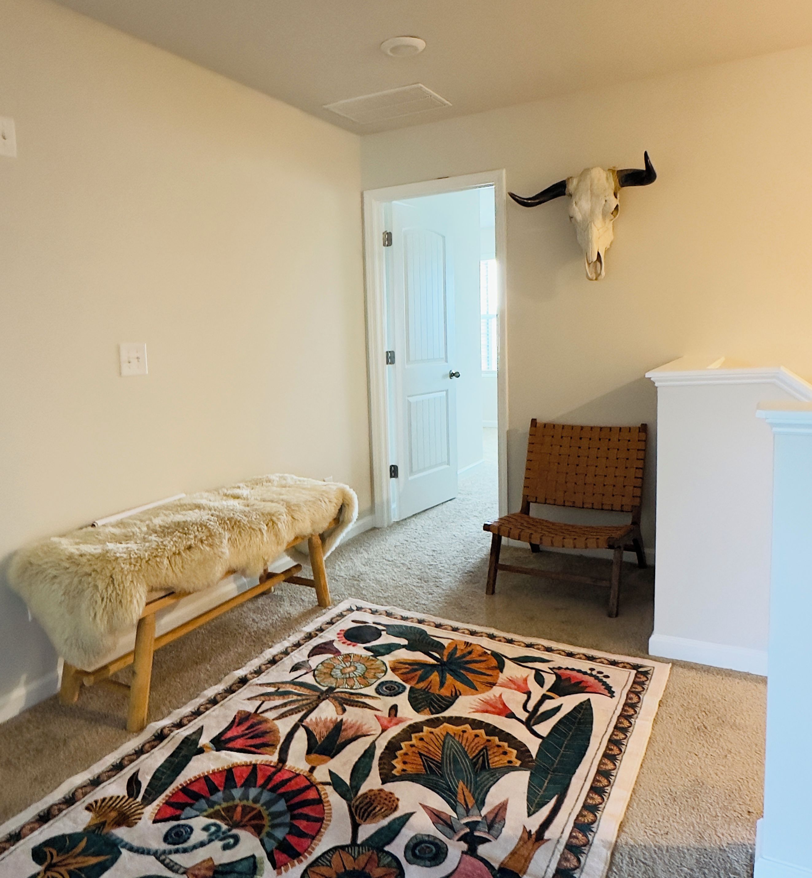 Una habitación con un banco cubierto de piel, una silla, un tapete decorativo y un cráneo de toro montado en la pared.