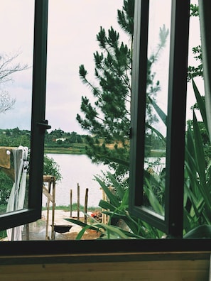 Blick durch ein Fenster auf einen See mit einem Holzsteg und viel Grün.