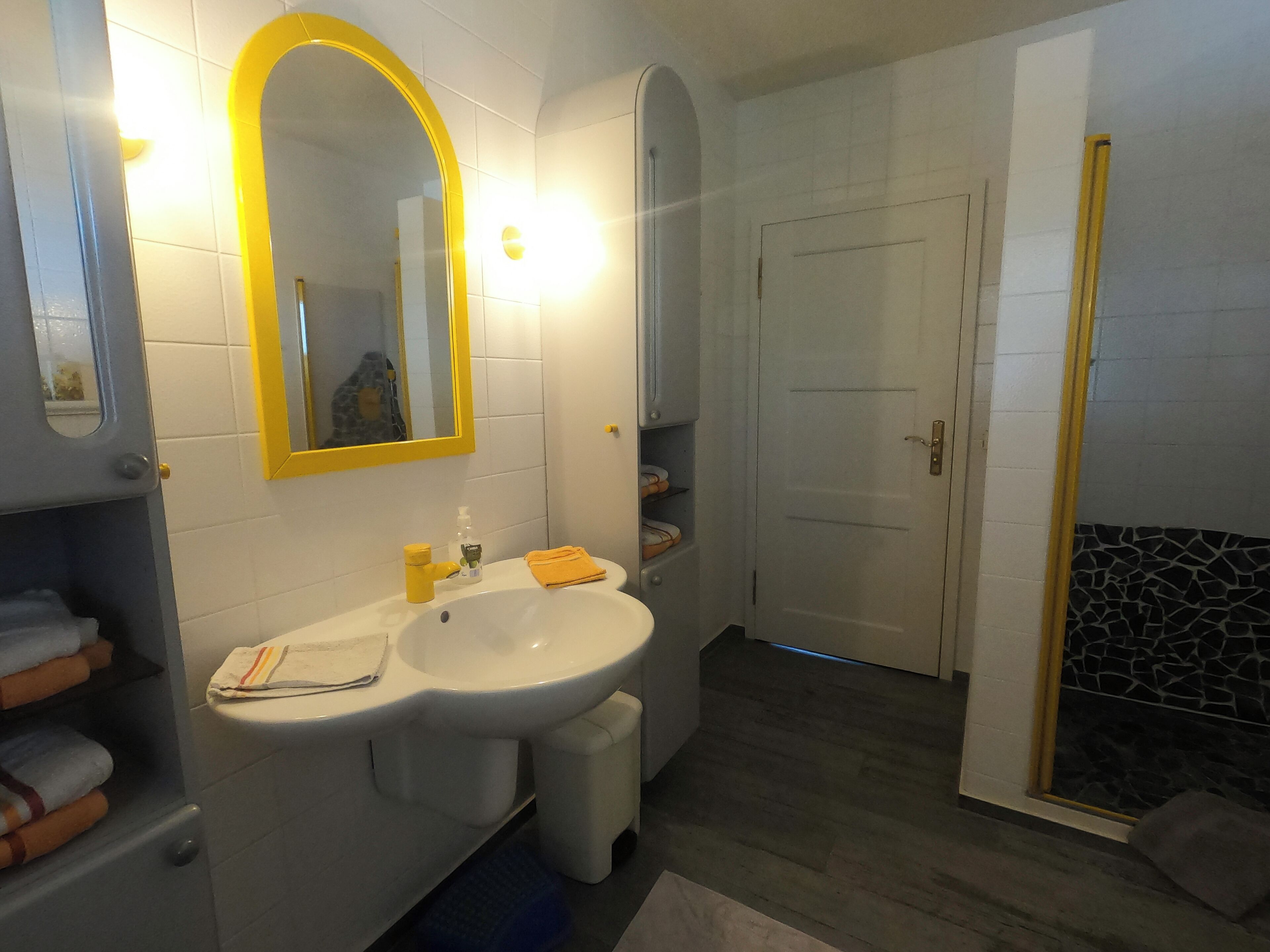 Ein Badezimmer mit Waschbecken, spiegel mit gelbem Rahmen und einer Dusche mit Steinwand.