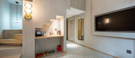 Un interior moderno con una escalera, un televisor de pantalla plana montado en la pared y un zapatero con varios pares de zapatos.