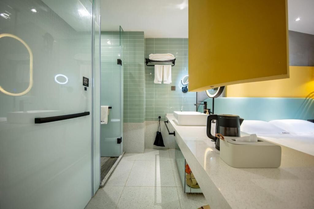 A modern bathroom with a glass shower enclosure, a sink with a coffee maker, and a towel rack.