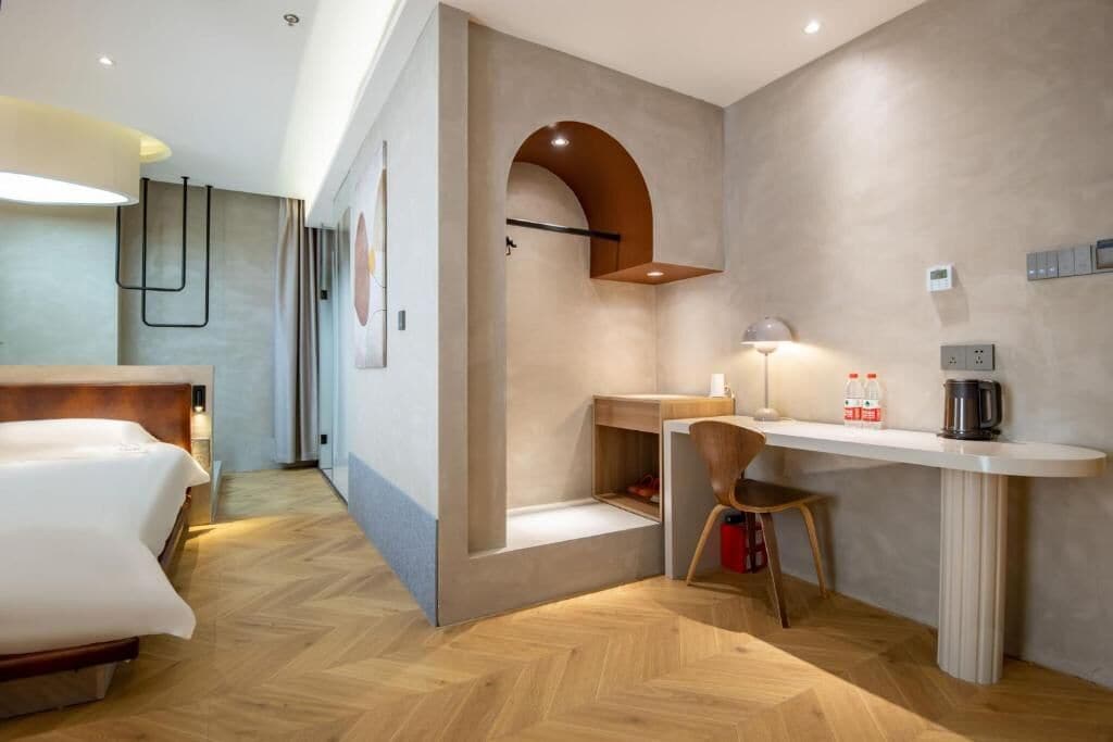 Una habitación de hotel moderna con cama, escritorio, silla y una pequeña zona de kitchenette.