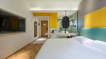 A modern hotel room with a large bed, a bathroom with a mirror and sink, and a window.