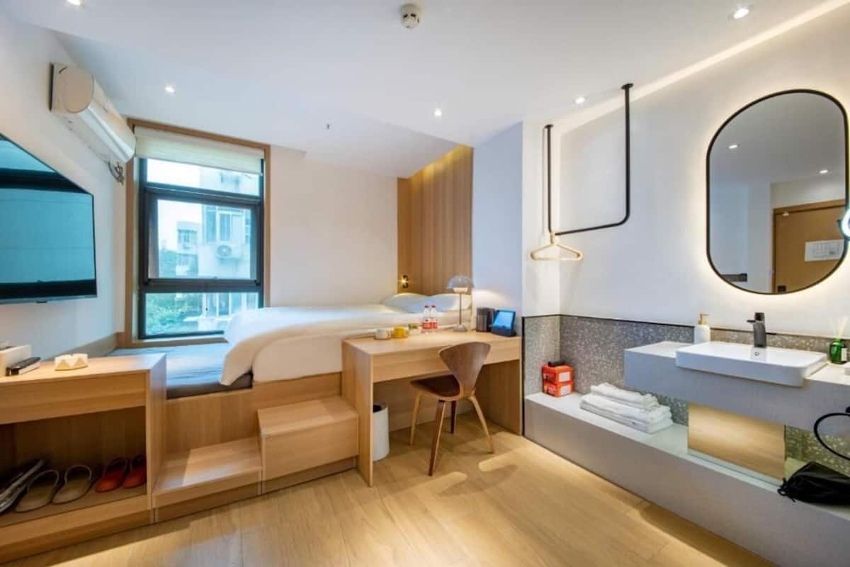 Una habitación de hotel moderna con cama, escritorio, silla y baño con lavamanos y espejo.