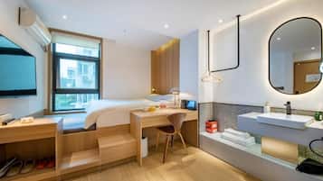 Una habitación de hotel moderna con cama, escritorio, silla y baño con lavamanos y espejo.