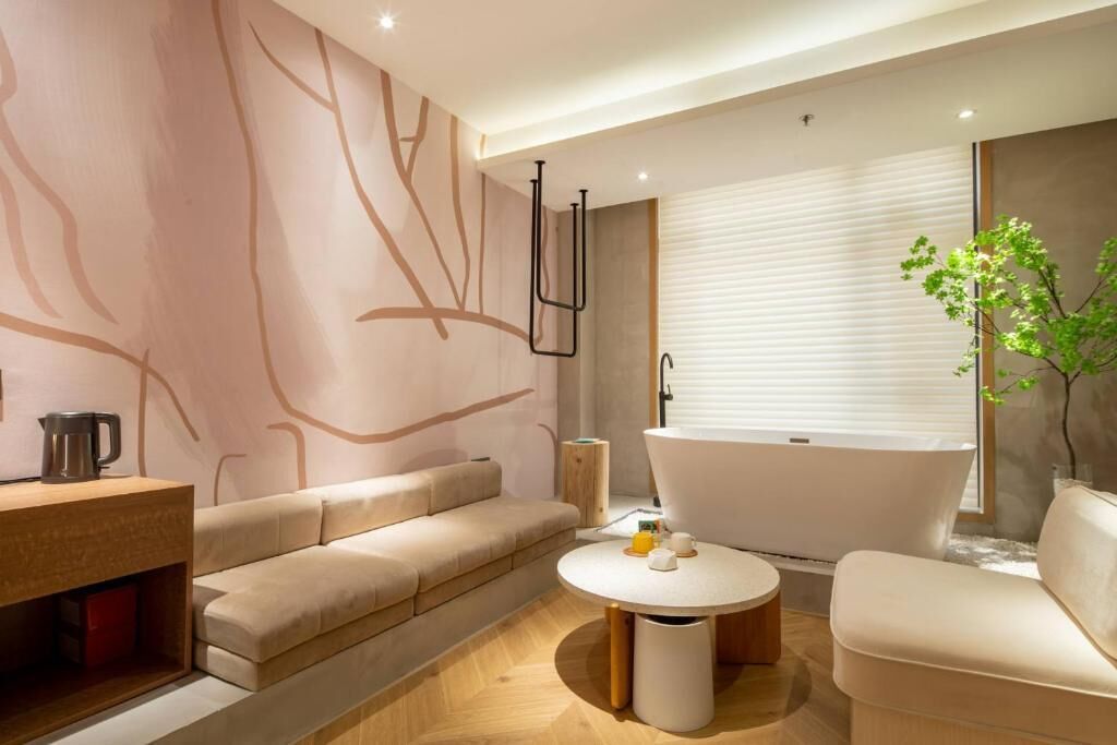 Ein modernes Badezimmer mit einer freistehenden Badewanne, einem hölzernen Waschtisch, einem beigefarbenen Sofa und einem runden Tisch mit einer Vase.