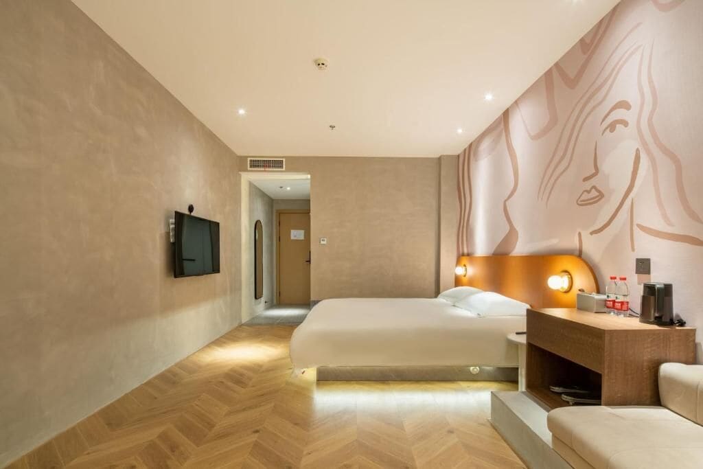 A modern hotel room with a large bed, a desk with a lamp, and a wall-mounted TV.