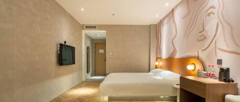Una habitación de hotel moderna con una cama grande, un escritorio con lámpara y un televisor montado en la pared.