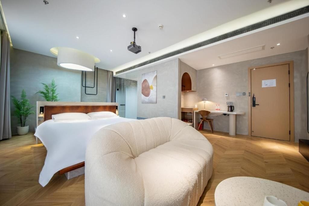 A modern hotel room with a large bed, a sofa, a desk, and a dining area.