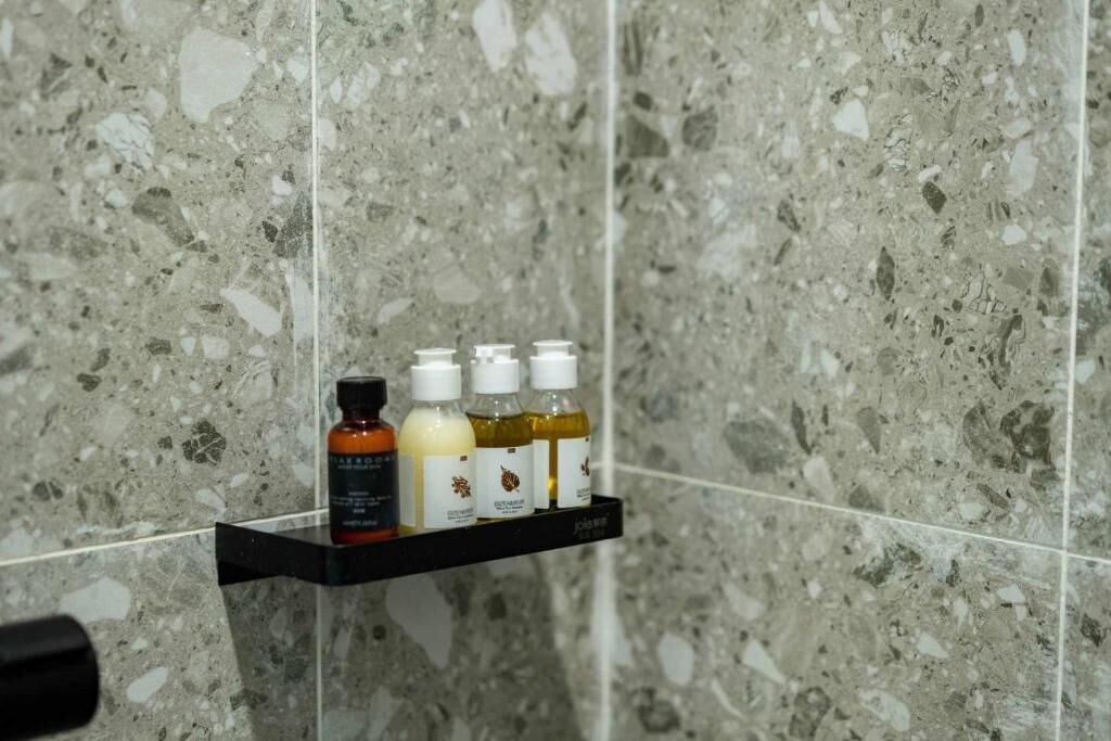 A bathroom with a marble wall and a shelf holding four bottles of toiletries.