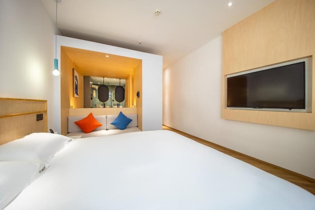 Une chambre d’hôtel moderne avec un grand lit, un téléviseur fixé au mur et un petit coin salon agrémenté de coussins.
