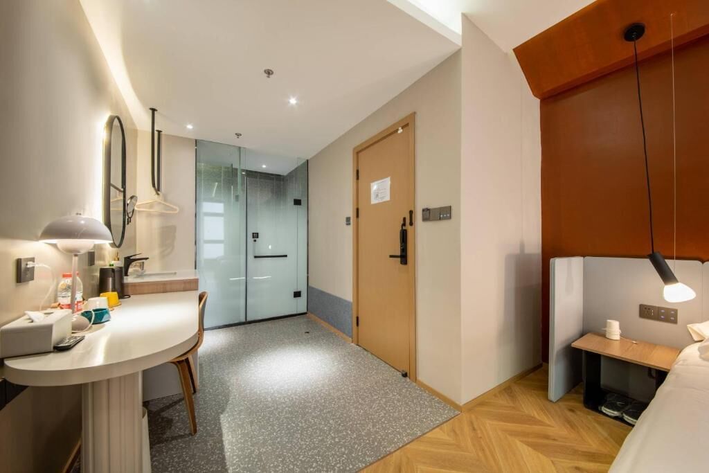 Een hotelkamer met een bed, een bureau met lamp, een stoel, een spiegel, een deur en een klein tafeltje met lamp.