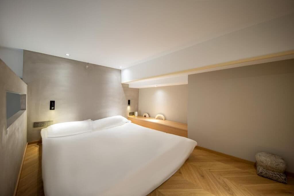 Una habitación de hotel moderna con una cama grande, piso de madera, escritorio empotrado y un pequeño rincón de descanso.