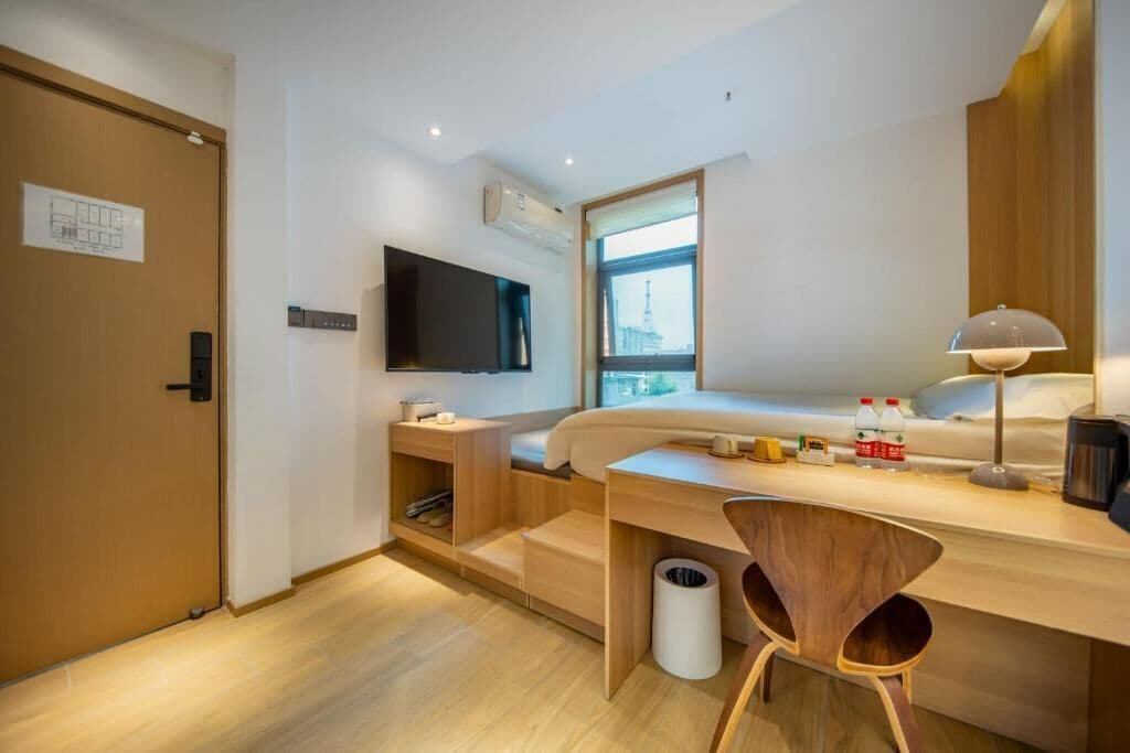 A modern hotel room with a bed, a desk, a chair, a TV, and a window with a view.