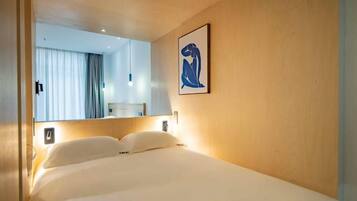 A hotel room with a bed, a wall-mounted artwork, and a mirror reflecting a bathroom.