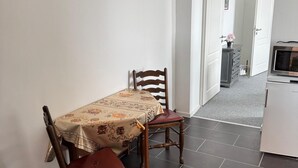 Ein Essbereich mit Tisch und Stühlen, eine Küche mit Kühlschrank und ein Flur, der zu einem weiteren Raum führt.