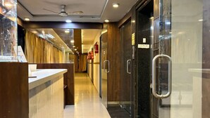 Eine Hotelhalle mit Empfangstresen, Glastür und Deckenventilator, sowie einem Feuerlöscher.