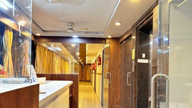 Eine Hotelhalle mit einer Rezeption, einer Glastrennwand, einem Deckenventilator und einem Feuerlöscher.