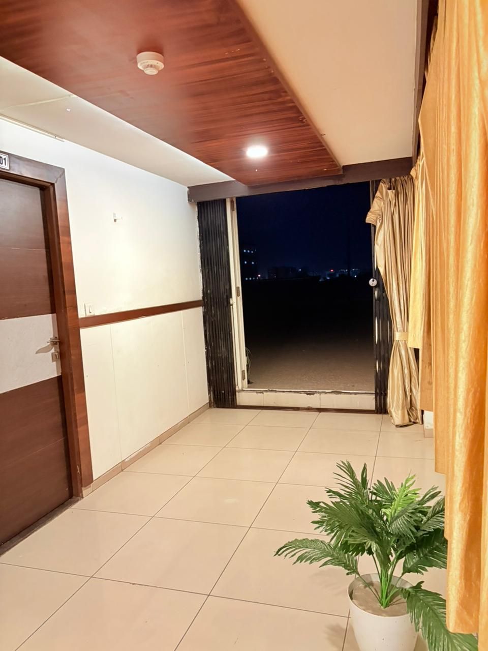 A room with a wooden ceiling, a sliding door, a potted plant, and a view of the night sky.
