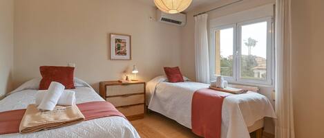 A hotel room with two beds, a nightstand, a lamp, a picture on the wall, and a window with curtains.